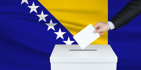 Election in Bosnia. The hand of man putting his vote in the ballot box. Waved Bosnia flag on...