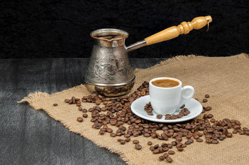Greek coffee in white small mug and vintage coffee pot. Turkish coffee cup with beans on wooden background. Coffee culture, traditional concept. Copy space for text.