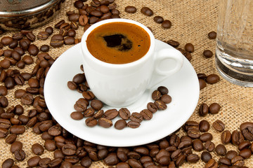 Cup of Greek coffee on sack background with coffee beans. Turkish coffee in white small mug. Traditional Greek coffee concept.