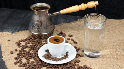 Hot coffee in Turkish Cooper and linen table. Greek Coffee Pot, Glass of water and Coffee beans dropped on wooden table. White small coffee mug. Traditional concept.