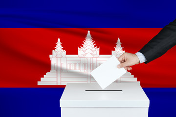Election in Cambodia. The hand of man putting his vote in the ballot box. Waved Cambodia flag on...