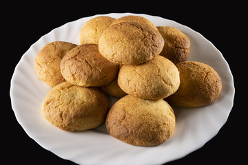  Pyramid of round biscuits, curved and gilded, arranged in a wavy white plate, on a black background