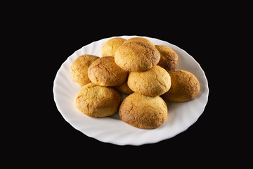  Pyramid of round biscuits, curved and gilded, arranged in a wavy white plate, on a black background