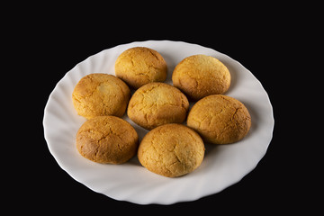  Round biscuits, curved and golden, arranged in a wavy white plate, on a black background