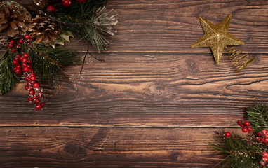 Christmas fir tree with berries pinecones and snow next to a gold christmas tree topper on wooden background