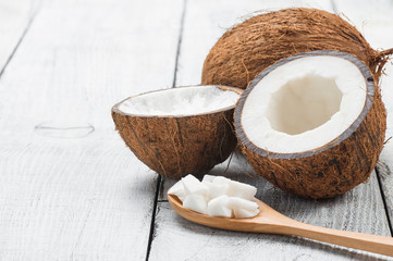 Organic natural whole and cracked coconut fruit and pieces of coconuts in wooden spoon on white wooden background, tropical healthy food concept, Cocos nucifera