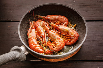 Close-up King prawns fried in a ceramic pan on a dark wooden table
