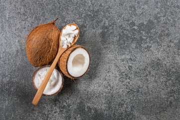 Organic natural whole and cracked coconut fruit and pieces of coconuts in wooden spoon on rustic background, tropical healthy food concept, Cocos nucifera