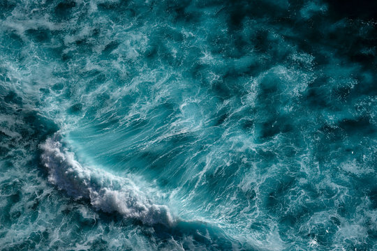 Aerial view to seething waves with foam backlit by the setting sun. Bali, Indonesia.