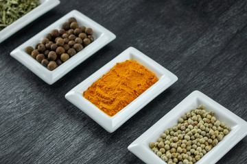 Spices and herbs on wooden table. Pepper, rosemary, tarragon, allspice, turmeric. Colorful spices in white bowls on grey background. Seasonings for cooking. Copy space for text.