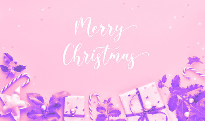 Festive monochrome pink and purple Christmas background with gift boxes, stripy candy canes, trinkets and decorative stars, geometric creative flat lay on pink paper, text 