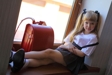 little schoolgirl in a school uniform and a backpack - obrazy, fototapety, plakaty