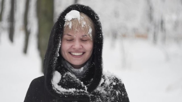Portrait of a happy young woman in the middle of a snowball fight getting a snowball in her face.