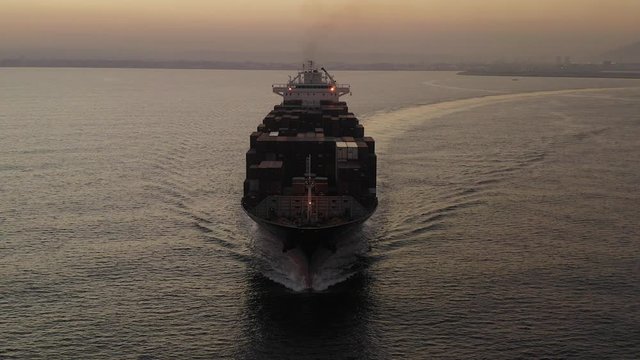 Large Container ship cruising slowly  across the open sea at Sunrise, Aerial follow footage.