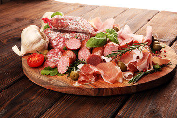 Food tray with delicious salami, pieces of sliced prosciutto crudo, sausage and basil. Meat platter