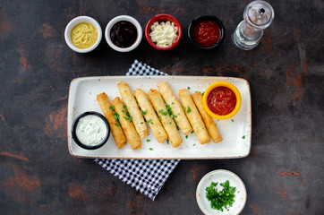 Cigarette Borek in white porcelain plate with various sauces on dark background. Top view
