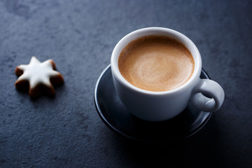Cup of coffee and Christmas cookie (cinnamon stars) on dark stone background. Close up. 
