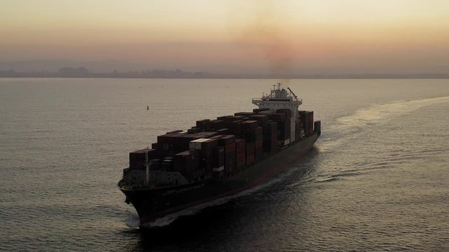 Large Container ship cruising slowly  across the open sea at Sunrise, Aerial follow footage.