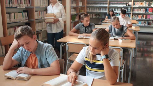 Schoolboys and girls preparing for lesson in school library, reading textbooks 