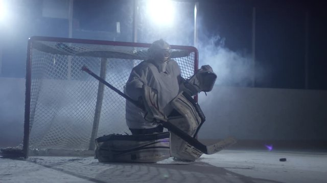 Front view of concentrated ice hockey goaltender standing in front of the net and catching puck on ice rink