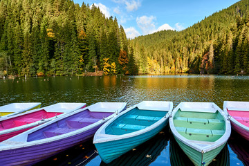 Multi-colored boats at the pier on Lake Lacu Rosu, Romania. Autumn landscape of mountain lake,...