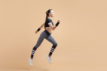 Fototapeta na wymiar A young attractive brunette girl runs with wireless headphones soaring above the ground, on a peach background, cardio.