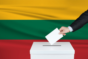 Election in Lithuania. The hand of man putting his vote in the ballot box. Waved Lithuania flag on...