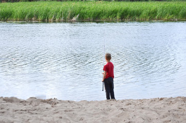 Fototapeta premium the boy is fishing by the river in summer, selective