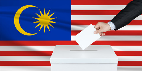 Election in Malaysia. The hand of man putting his vote in the ballot box. Waved Malaysia flag on background.