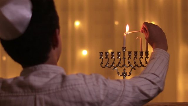 rear view of a young boy lights a second menorah candle during the Jewish holiday of Hanukkah.