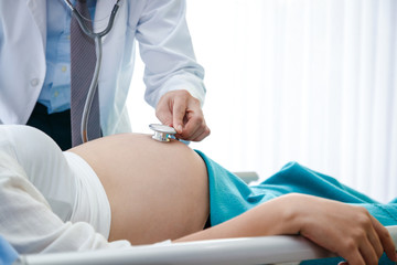 The doctor used a bell-shaped stethoscope to check the pregnancy of a woman lying in a bed in a clinic.