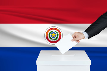 Election in Paraguay. The hand of man putting his vote in the ballot box. Waved Paraguay flag on background.