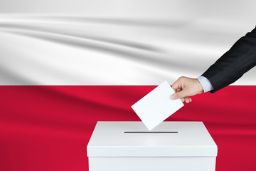 Election in Poland. The hand of man putting his vote in the ballot box. Waved Poland flag on...