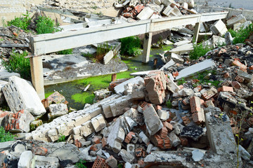 Heap of debris of the destroyed building. The pieces of brick, concrete, stones, expanded clay are destroyed. A swamp with a green slime in a ruined building.