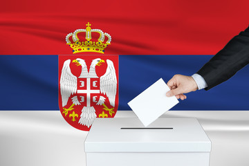 Election in Serbia. The hand of man putting his vote in the ballot box. Waved Serbia flag on background.
