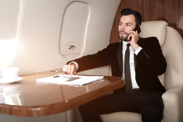 Businessman talking by phone on board the modern private airplane