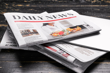 Newspapers and laptop on dark wooden background, closeup