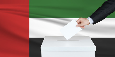 Election in United Arab Emirates. The hand of man putting his vote in the ballot box. Waved United Arab Emirates flag on background.
