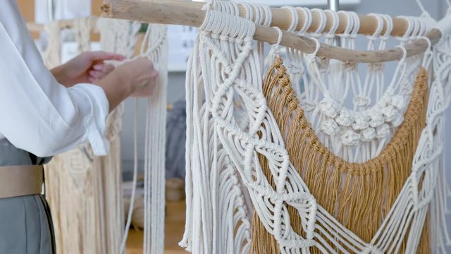 finished macrame on a stick on the background of a woman weaving macrame
