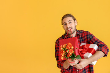 Handsome man with flowers and gifts on color background. Valentine's Day celebration