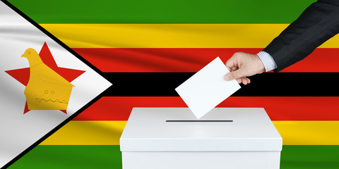 Election in Zimbabwe. The hand of man putting his vote in the ballot box. Waved Zimbabwe flag on...