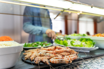 Plate of prawns and salad with a boy catching unfocused food in the background of a self-service