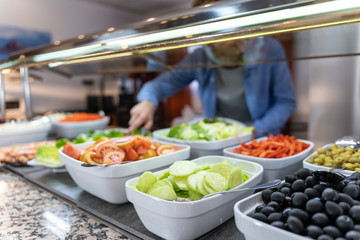 Plates of healthy food, olives and salad and an unfocused background man picking up food.