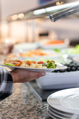 Vertical photo of a woman holding a plate of food with one hand in a self-service restaurant