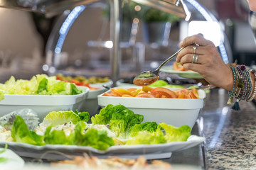 Hand with ring picking up food from a salad plate at a self-service restaurant counter