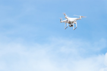 White Quad Copter drone hovering and flying with bright blue sky space for copy text.