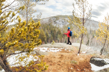 hiker man with a backpack stands on top of a mountain above the forest and looks at the valley