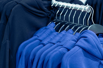 Fototapeta premium The trend color of the year 2020 Classic Blue. Hoodies on hangers in a clothing store, close up.