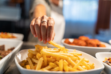 Detail of a hand with a ring taking a potato from a plate of chips in a restaurant