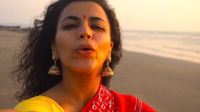 portrait of attractive indian woman in sari smiling brunette confident pretty,touching hair and feeling good recording video on the phone camera and wawing hand